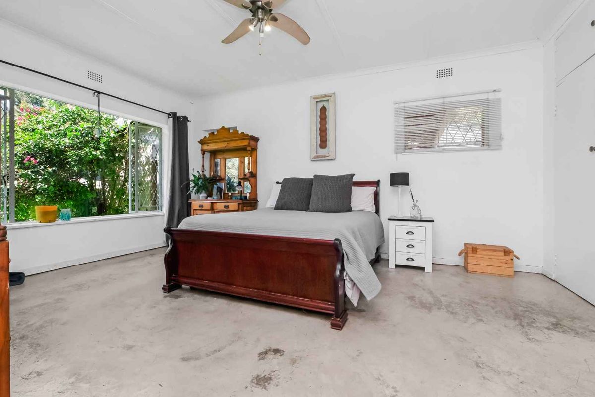 A spacious bedroom featuring large windows, a ceiling fan, and exposed concrete flooring, offering a blank canvas for potential renovation and interior design updates.