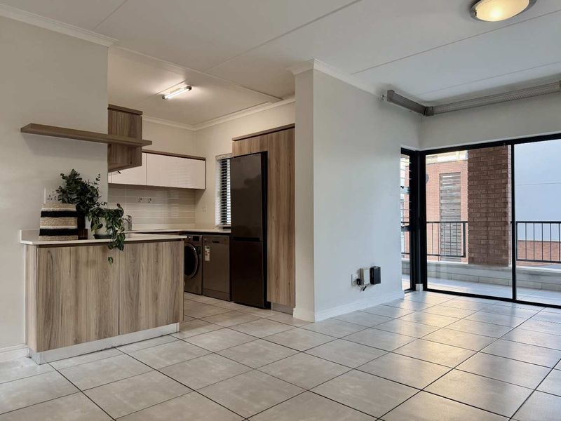 Open-plan living area featuring modern wood-finish cabinetry, tiled flooring, and a sliding glass door leading to a balcony.