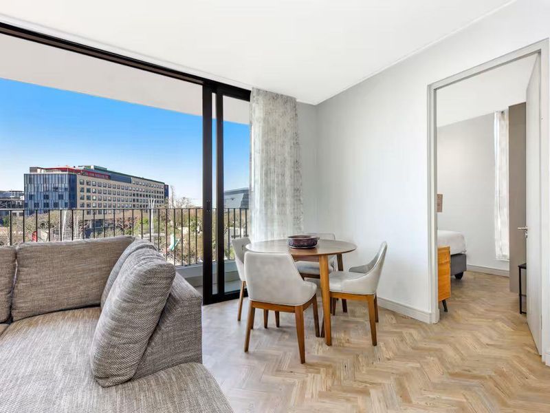 Bright open-plan living area featuring elegant herringbone timber flooring and large sliding glass doors opening onto a private balcony with urban views.
