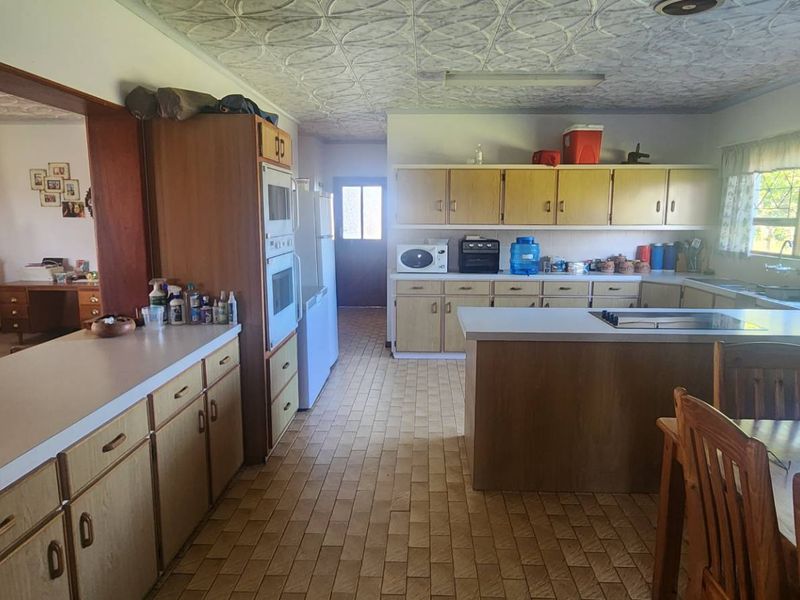 Spacious open-plan kitchen featuring dated cabinetry, laminate countertops, built-in appliances, and tiled flooring, offering significant potential for a modern renovation.