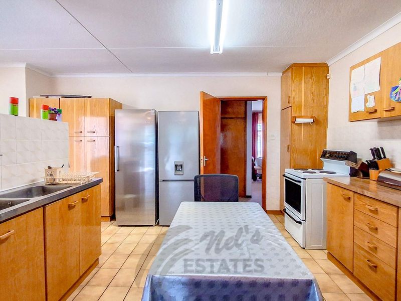 A functional kitchen featuring wooden cabinetry, tiled flooring, a double sink, and a freestanding stove, offering a practical layout with potential for modernization.
