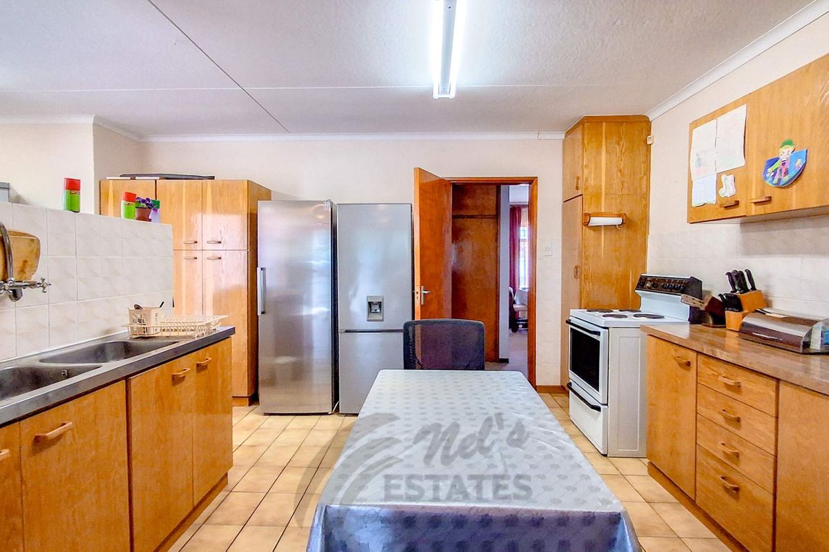 A functional kitchen featuring wooden cabinetry, tiled flooring, a double sink, and a freestanding stove, offering a practical layout with potential for modernization.