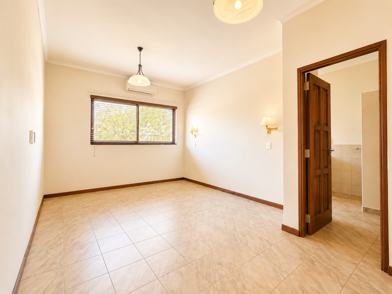 A bright, empty bedroom featuring tiled flooring, a split-system air conditioner, and direct access to an adjoining bathroom.
