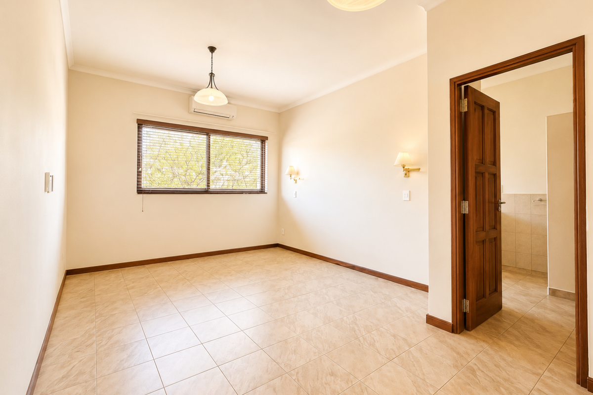 A bright, empty bedroom featuring tiled flooring, a split-system air conditioner, and direct access to an adjoining bathroom.