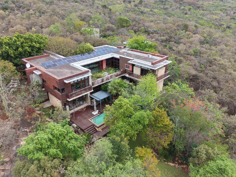 Aerial view of a multi-level modern residence featuring solar panels, a swimming pool, and extensive wooden decking nestled in a natural landscape.