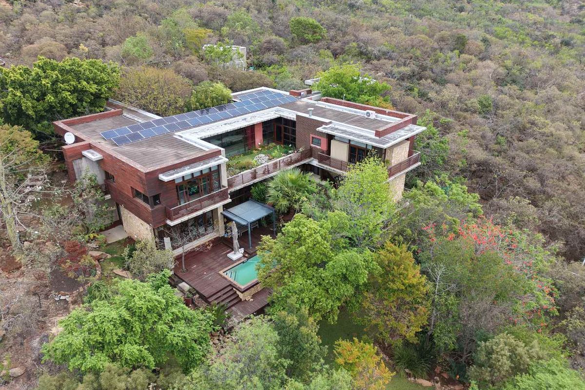 Aerial view of a multi-level modern residence featuring solar panels, a swimming pool, and extensive wooden decking nestled in a natural landscape.