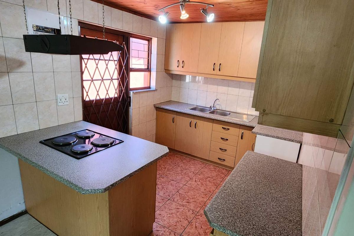 Functional kitchen featuring laminate cabinetry, a built-in hob on a breakfast counter, double sink, and tiled splashbacks.