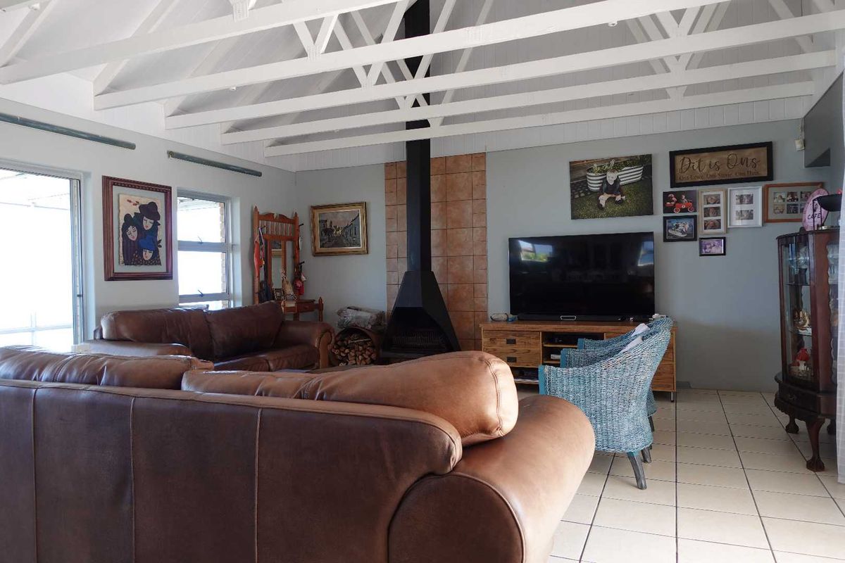 Spacious living room featuring a vaulted ceiling with exposed beams and a central freestanding fireplace with tiled surround and ceramic floor tiles.