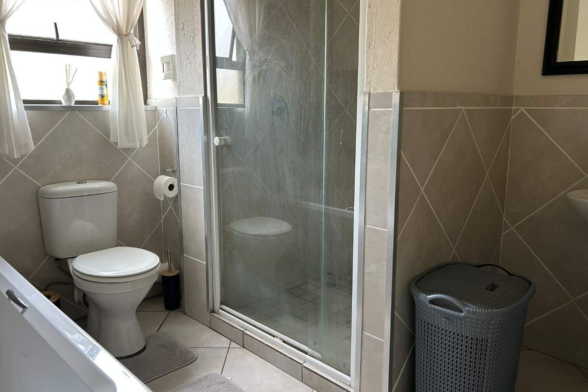 A functional bathroom featuring a shower enclosure, bathtub, and toilet with neutral wall and floor tiling.