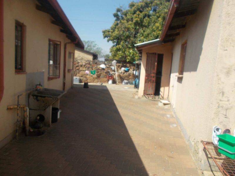 A paved rear courtyard area featuring a concrete utility sink, security gate, and stone boundary wall, showing signs of wear and weathering.