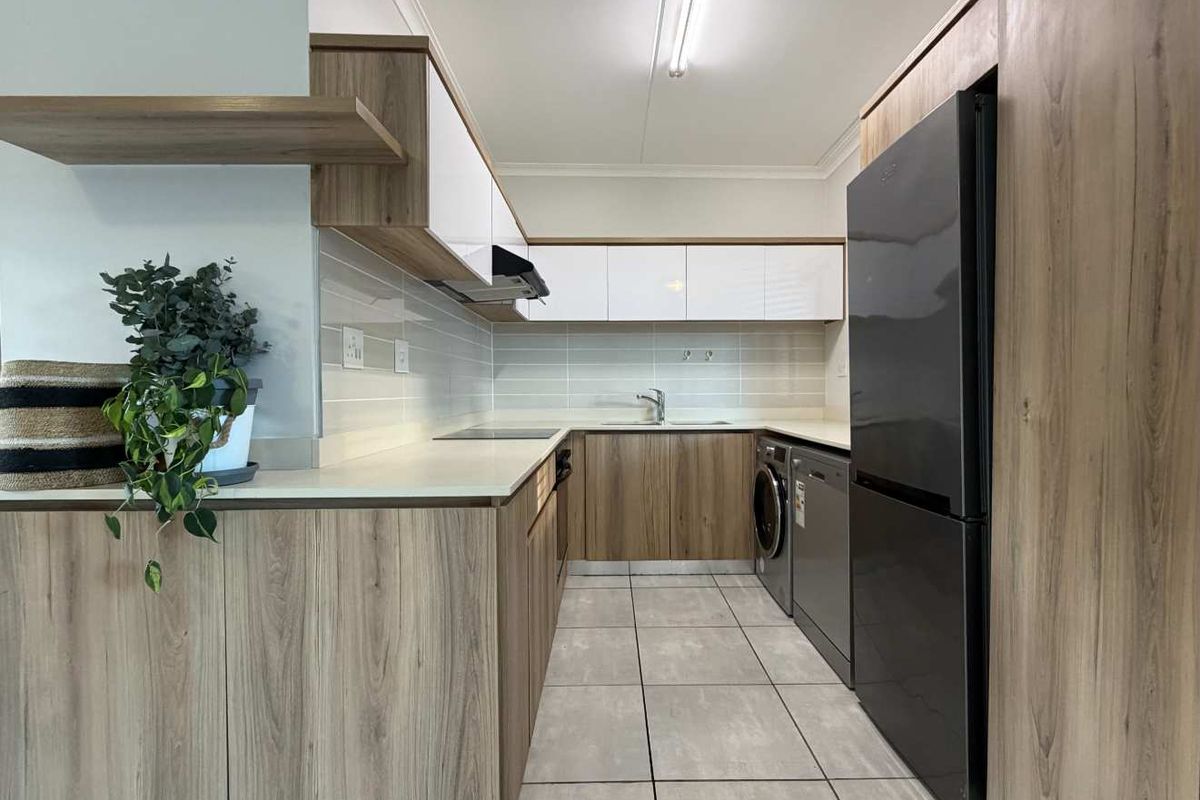 Modern kitchen featuring wood-grain cabinetry, white high-gloss upper cabinets, stone countertops, tiled backsplash, and integrated appliance spaces with neutral floor tiling.