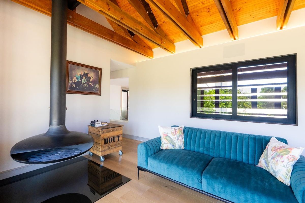 A bright living room featuring exposed timber ceiling beams, light wood flooring, and a modern suspended black fireplace.