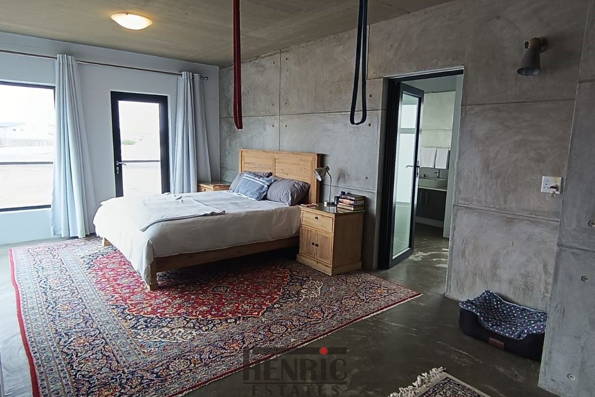 Spacious bedroom featuring industrial-style exposed concrete walls and ceilings, polished concrete flooring, and direct access to an en-suite bathroom.