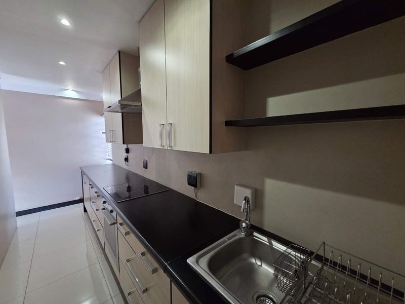 A modern, clean kitchen featuring light wood-tone cabinetry, dark countertops, integrated appliances, and sleek floating shelves, offering a functional and minimalist workspace.