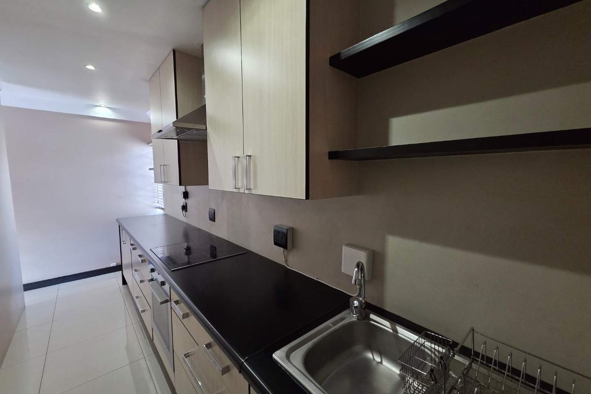 A modern, clean kitchen featuring light wood-tone cabinetry, dark countertops, integrated appliances, and sleek floating shelves, offering a functional and minimalist workspace.