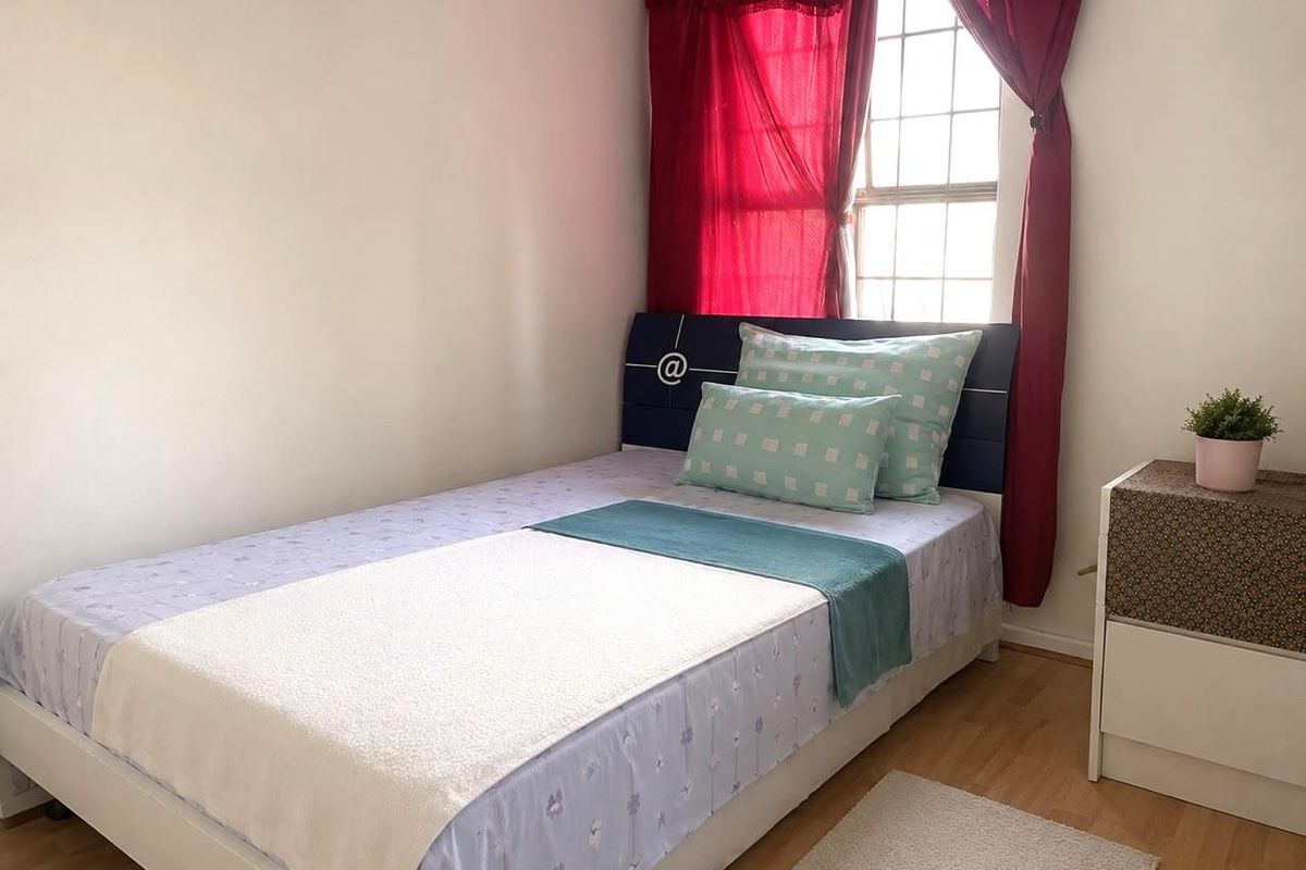 A functional bedroom featuring laminate flooring and a grid-pattern window, providing natural light to the space.