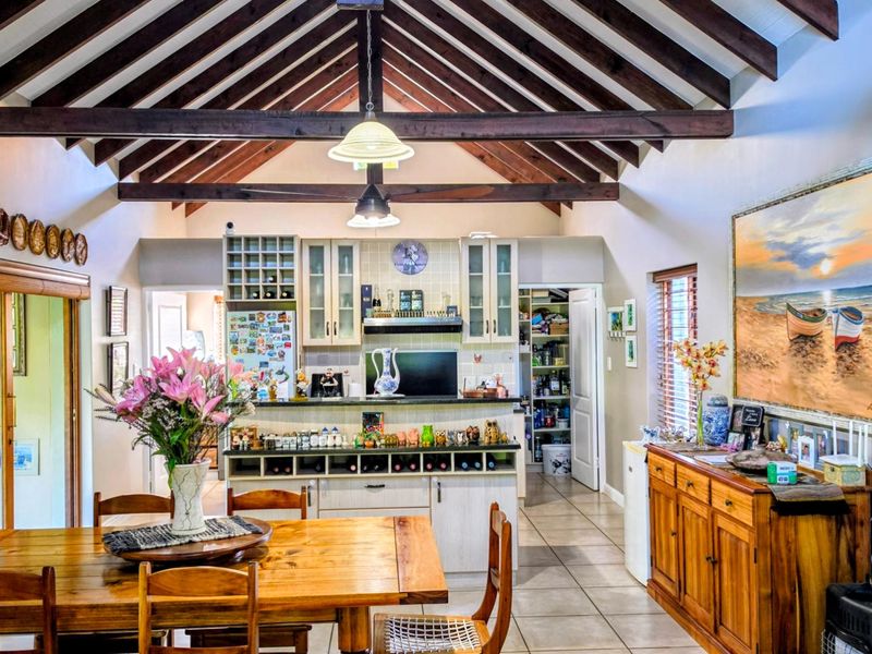 Spacious open-plan living and dining area featuring a striking vaulted ceiling with exposed timber beams, tiled flooring, and a well-appointed kitchen with pantry.