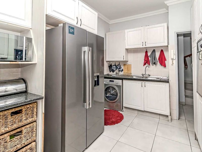 A functional kitchen featuring white cabinetry, tiled backsplash, built-in oven, microwave, and integrated laundry space with tiled flooring.