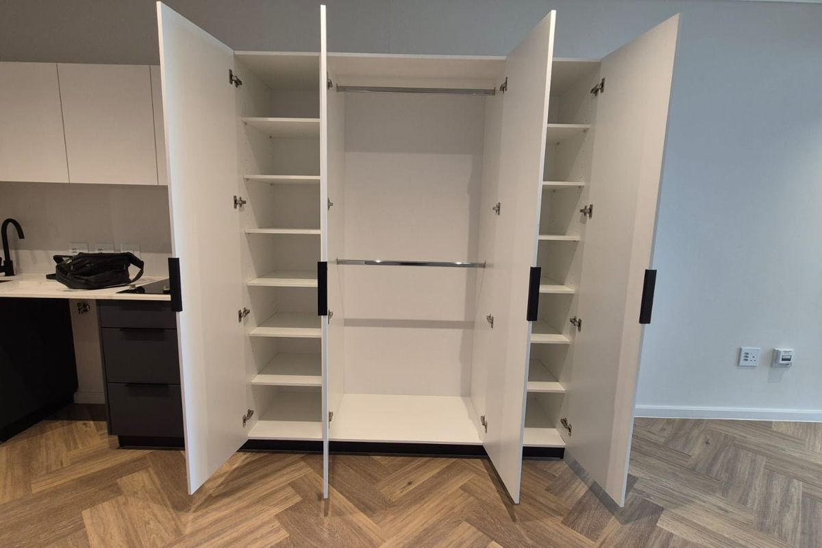A modern, built-in white wardrobe with integrated shelving and hanging rails, featuring clean lines and contemporary design.