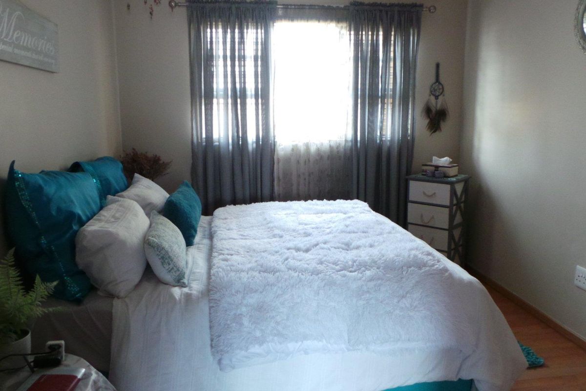A cozy bedroom featuring laminate flooring, a window with curtain tracks, and standard electrical outlets.