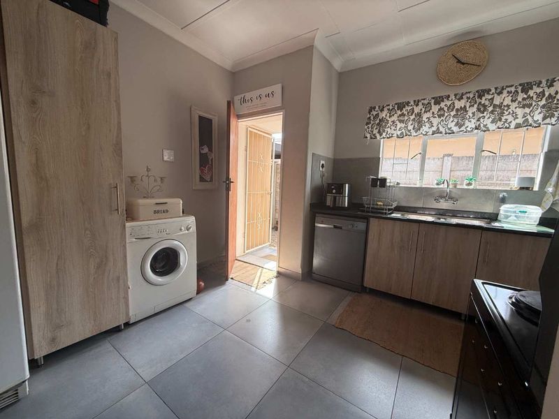 Functional kitchen featuring light wood-finish cabinetry, tiled flooring, and direct access to an outdoor area through a security gate.