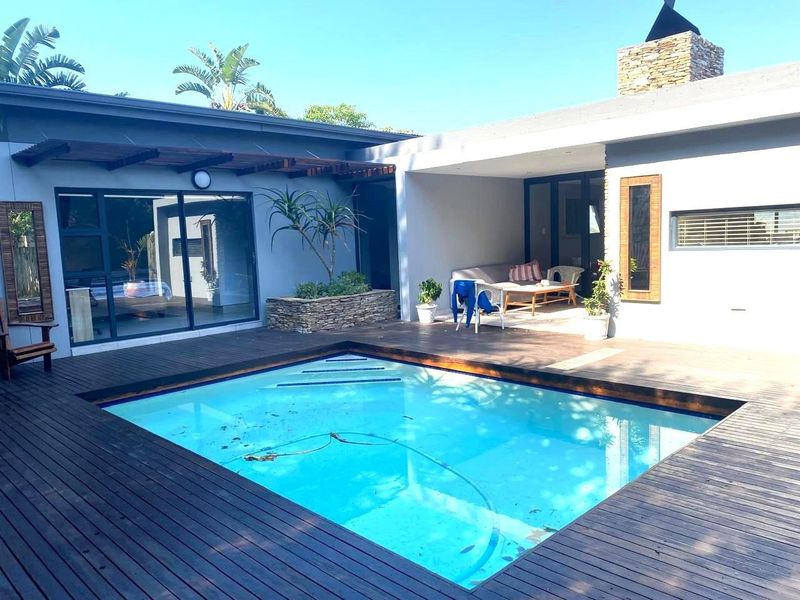 Outdoor entertainment area featuring a swimming pool with timber decking, a covered patio, and a stone-clad chimney feature.