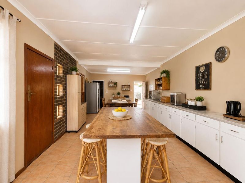 Spacious kitchen featuring white cabinetry, laminate countertops, tiled flooring, and a distinctive exposed brick feature wall with integrated shelving.