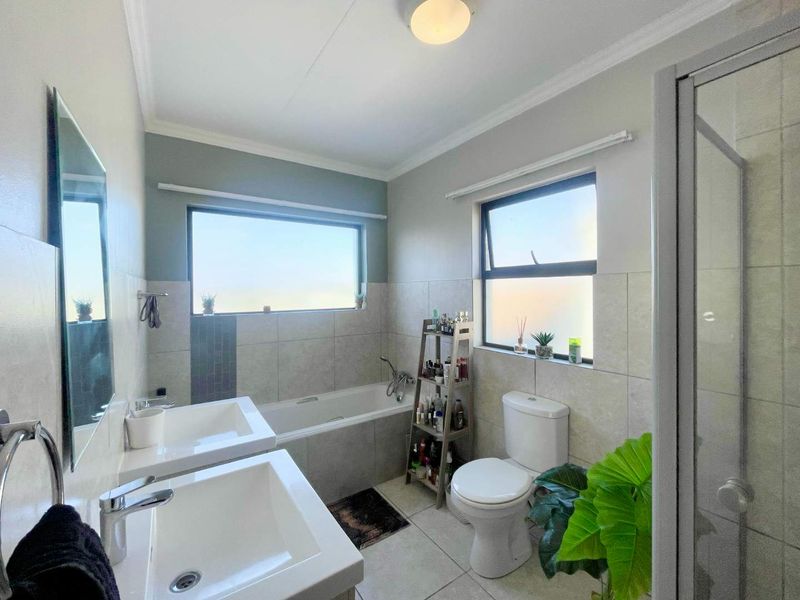 A modern, well-lit bathroom featuring a double vanity, a built-in bathtub, a separate shower enclosure, and neutral tiled finishes.
