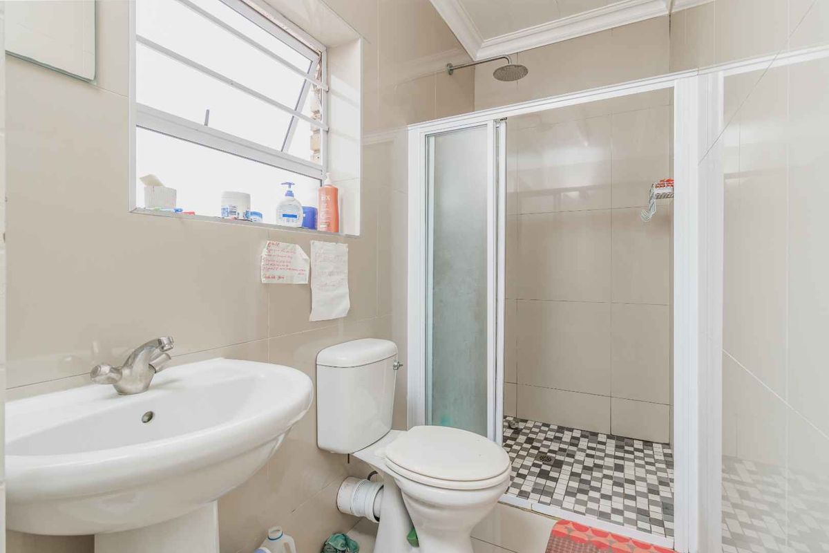 A functional bathroom featuring a pedestal sink, a standard toilet, and a walk-in shower enclosure with tiled walls and flooring.
