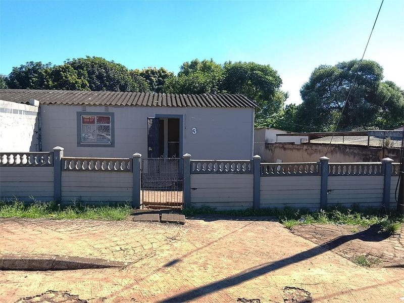 Front exterior view of a single-story house featuring a precast concrete boundary wall, metal security gate, and a corrugated roof.