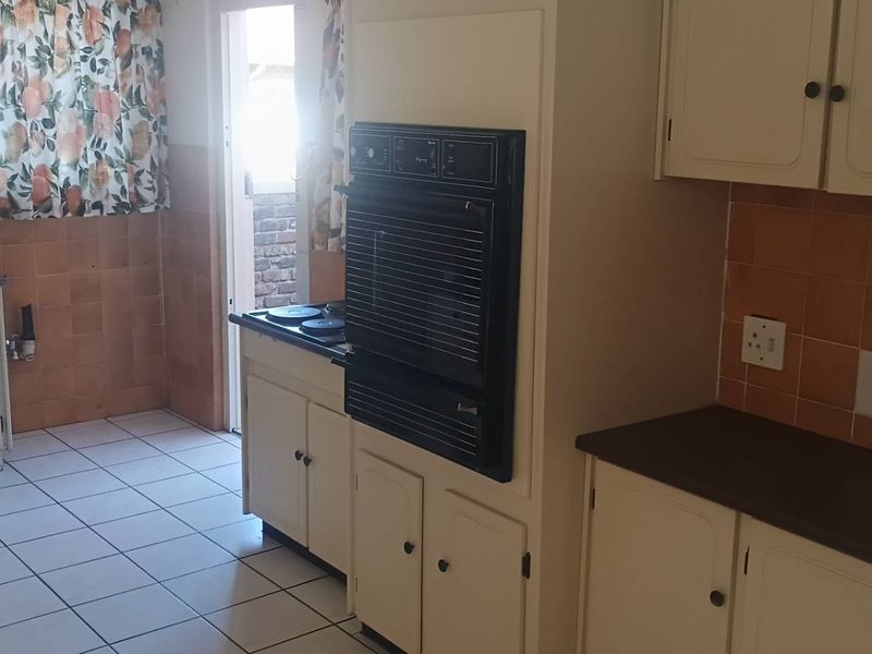 A dated kitchen featuring built-in cabinetry, a double sink, integrated oven, and hob with tiled backsplash and flooring.