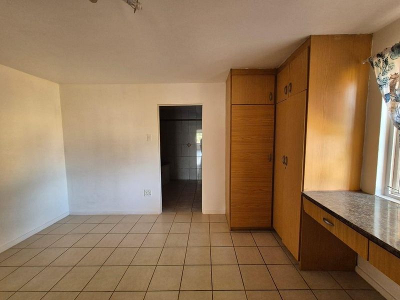 A vacant bedroom featuring built-in wooden cupboards, a matching built-in desk, and neutral tiled flooring, with direct access to an adjoining bathroom.
