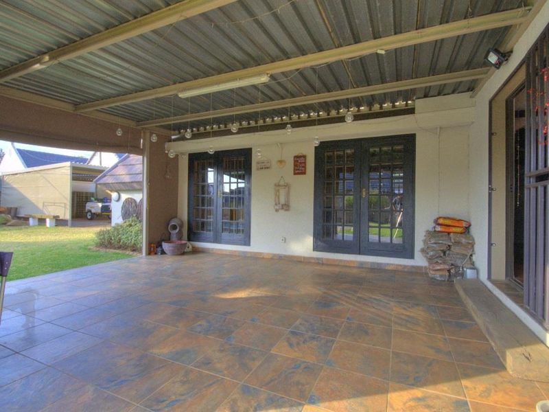 A spacious covered patio featuring tiled flooring, corrugated metal roofing, and double french doors leading into the home.