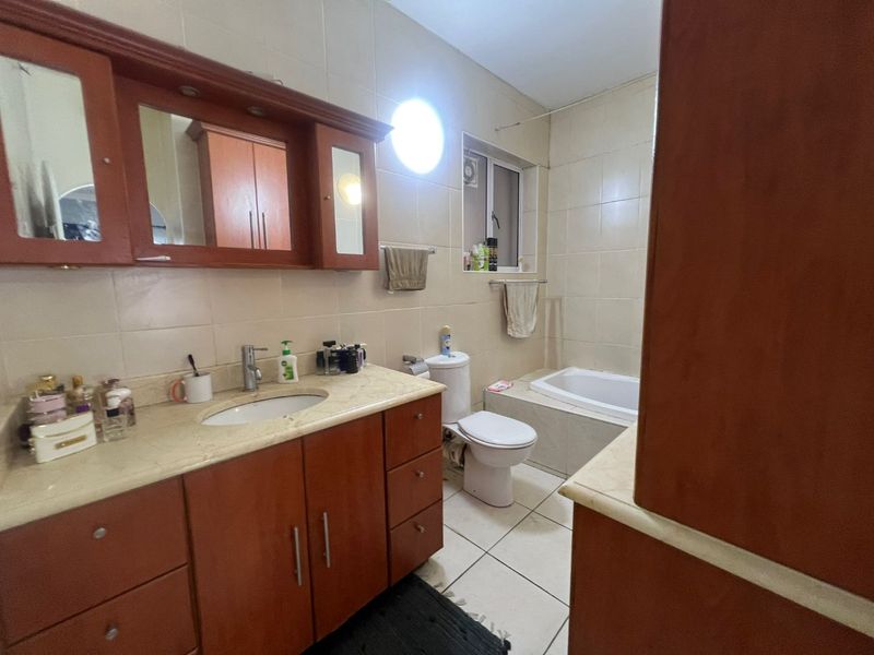 A functional bathroom featuring a built-in bathtub, vanity cabinet with integrated basin, and wall-mounted mirror cabinet, finished with neutral wall and floor tiles.