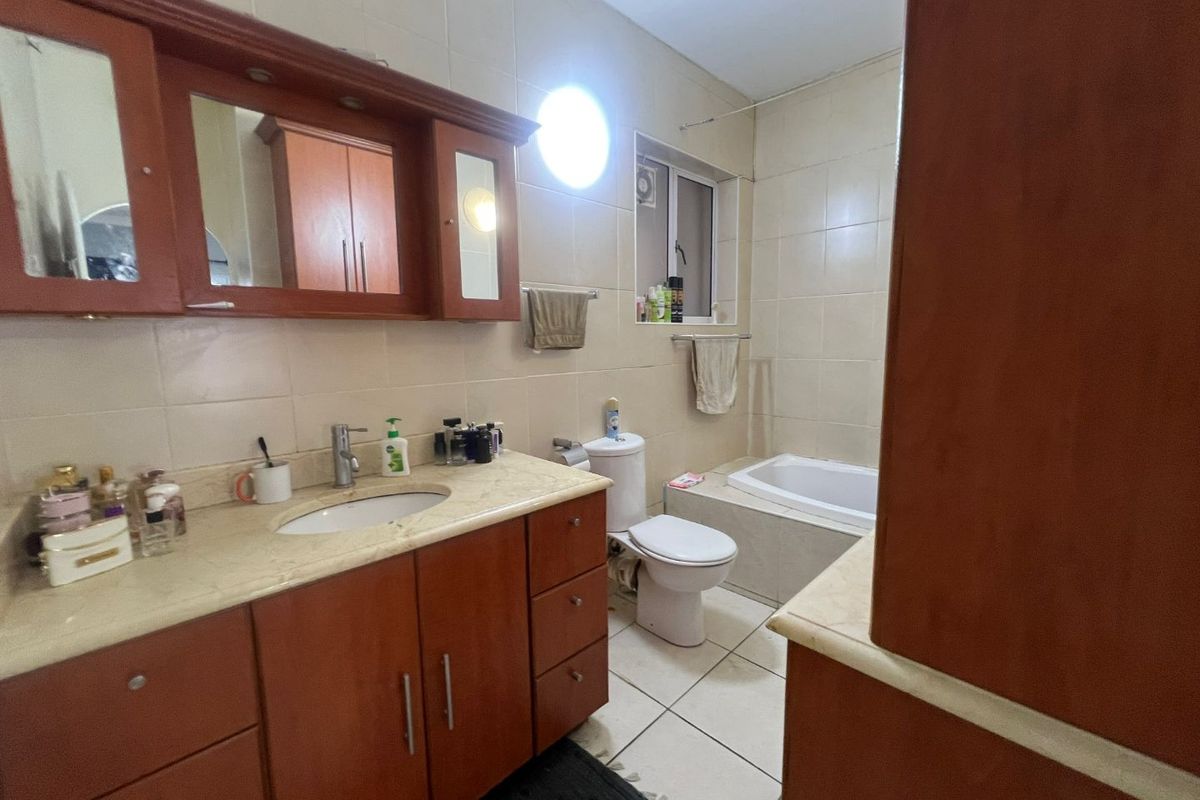 A functional bathroom featuring a built-in bathtub, vanity cabinet with integrated basin, and wall-mounted mirror cabinet, finished with neutral wall and floor tiles.
