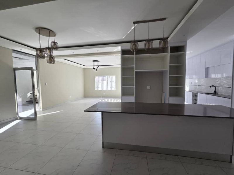 Spacious open-plan living and kitchen area featuring modern cabinetry, a large central island, tiled flooring, and contemporary pendant lighting throughout.