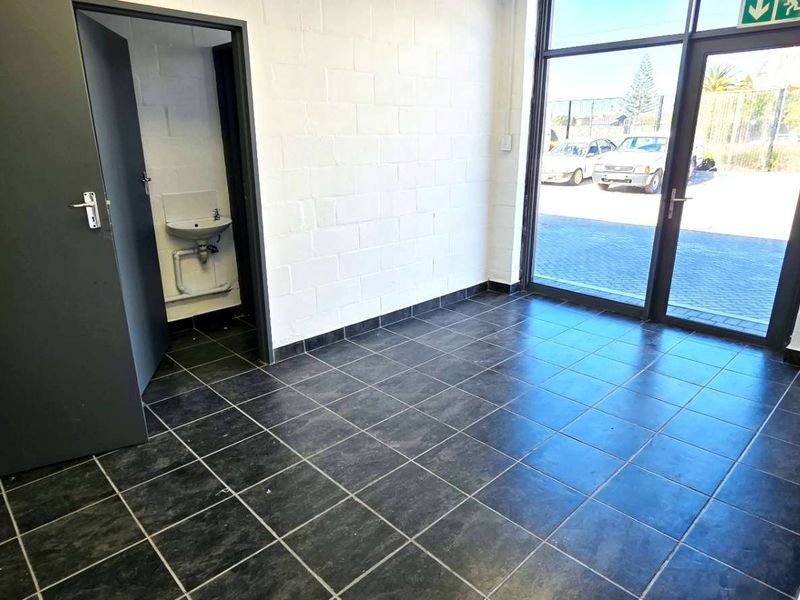 A clean, industrial-style entrance area featuring dark tiled flooring, exposed blockwork walls, and a glass-panelled door leading to the exterior.
