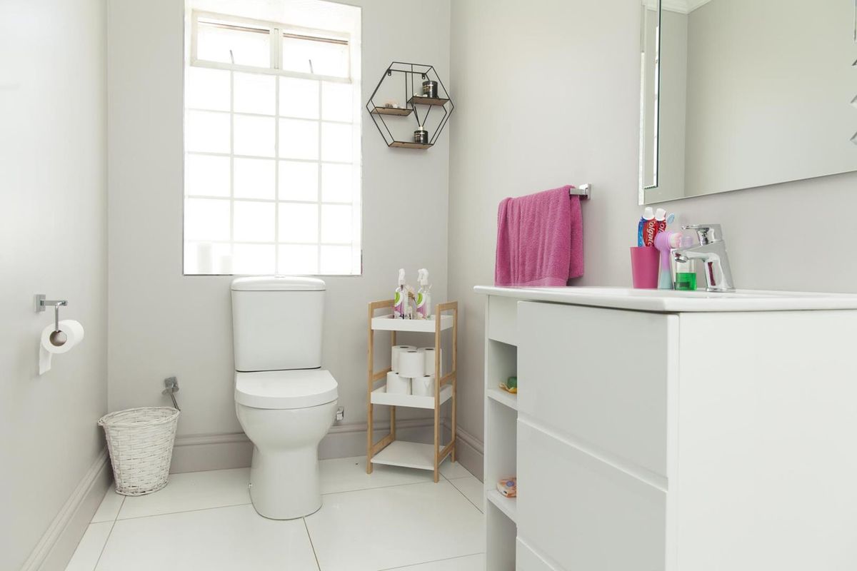 A clean and functional bathroom featuring a white vanity, modern toilet, and a glass block window providing natural light.