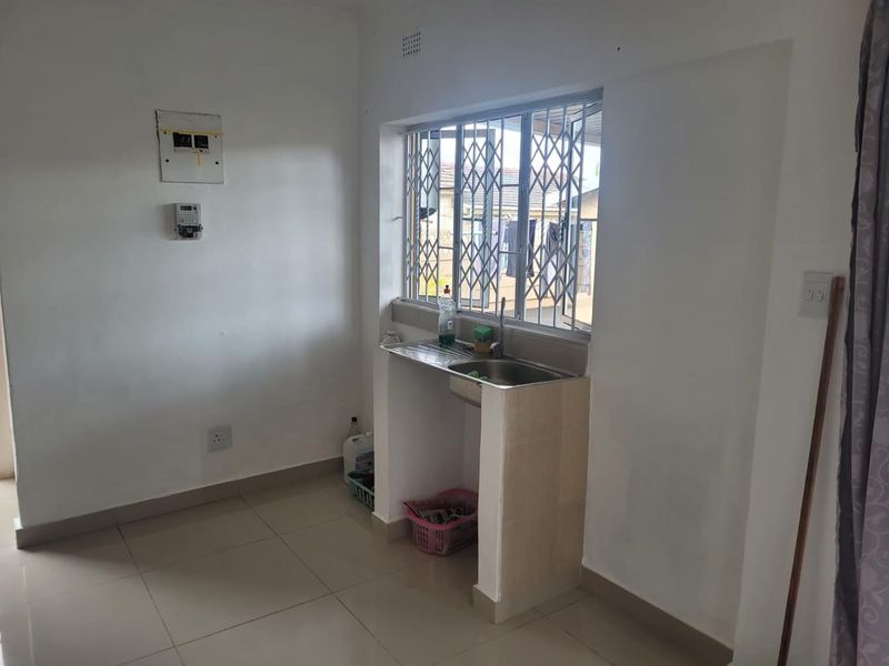 A compact kitchen area featuring a single stainless steel sink, tiled flooring, and a security gate over the window.
