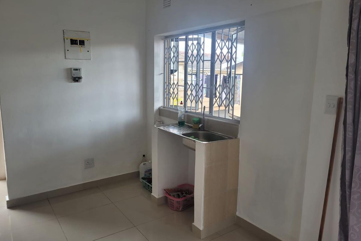 A compact kitchen area featuring a single stainless steel sink, tiled flooring, and a security gate over the window.
