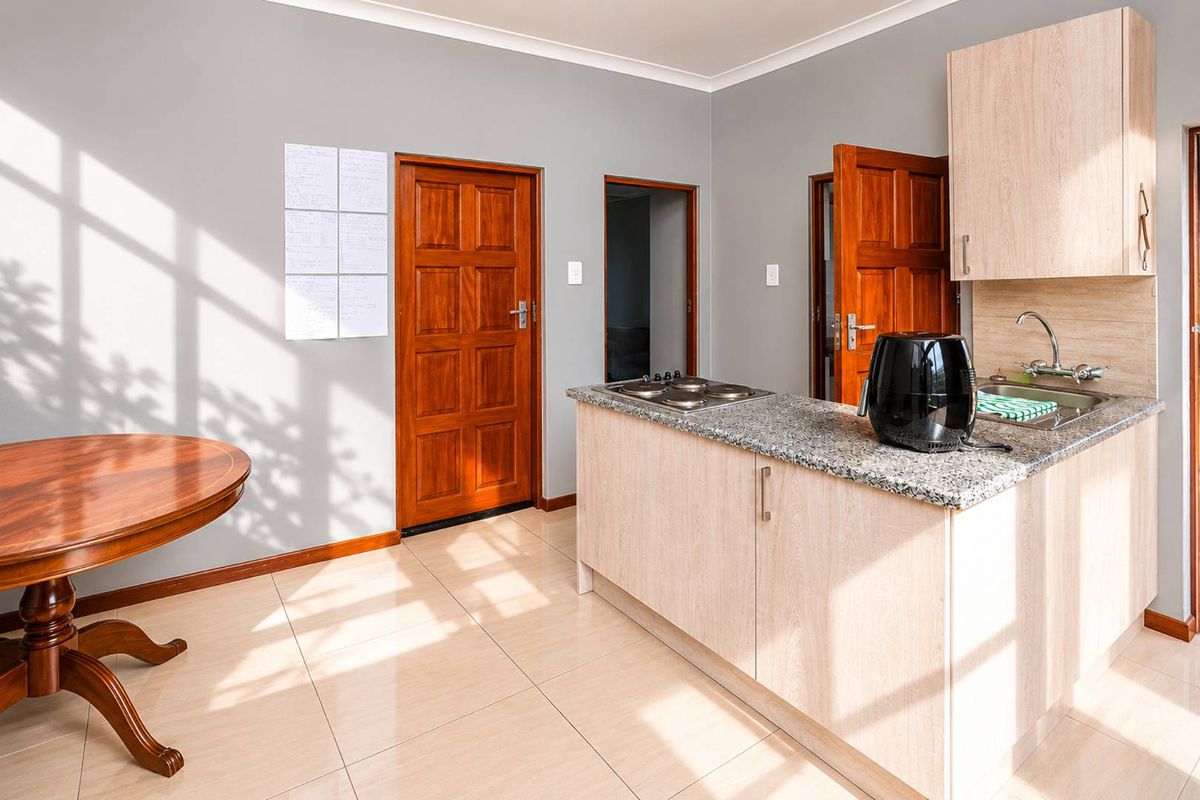A compact kitchen area featuring light wood cabinetry, granite countertops, a built-in hob, and a stainless steel sink, finished with neutral floor tiles.