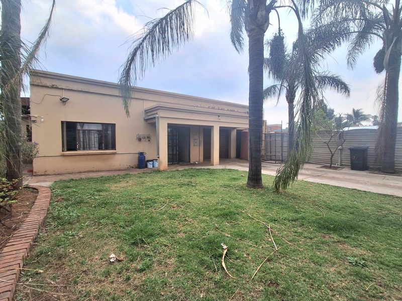 Rear view of the property featuring a paved driveway, covered patio area, and a garden with established palm trees.