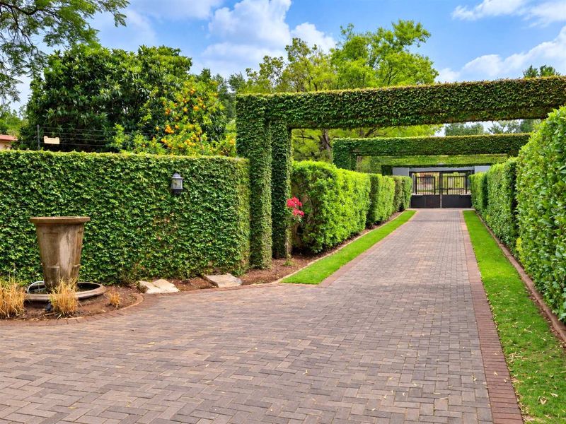 A beautifully landscaped driveway featuring manicured hedge archways, a stone fountain, and a secure gated entrance, providing an elegant approach to the property.
