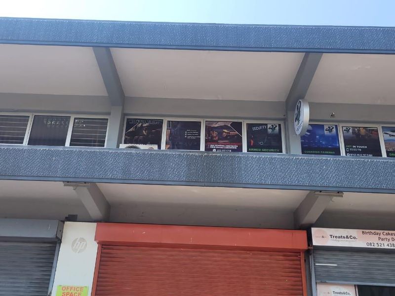 Front elevation of a commercial building featuring ground-level roller shutter doors and upper-level office windows with business signage.