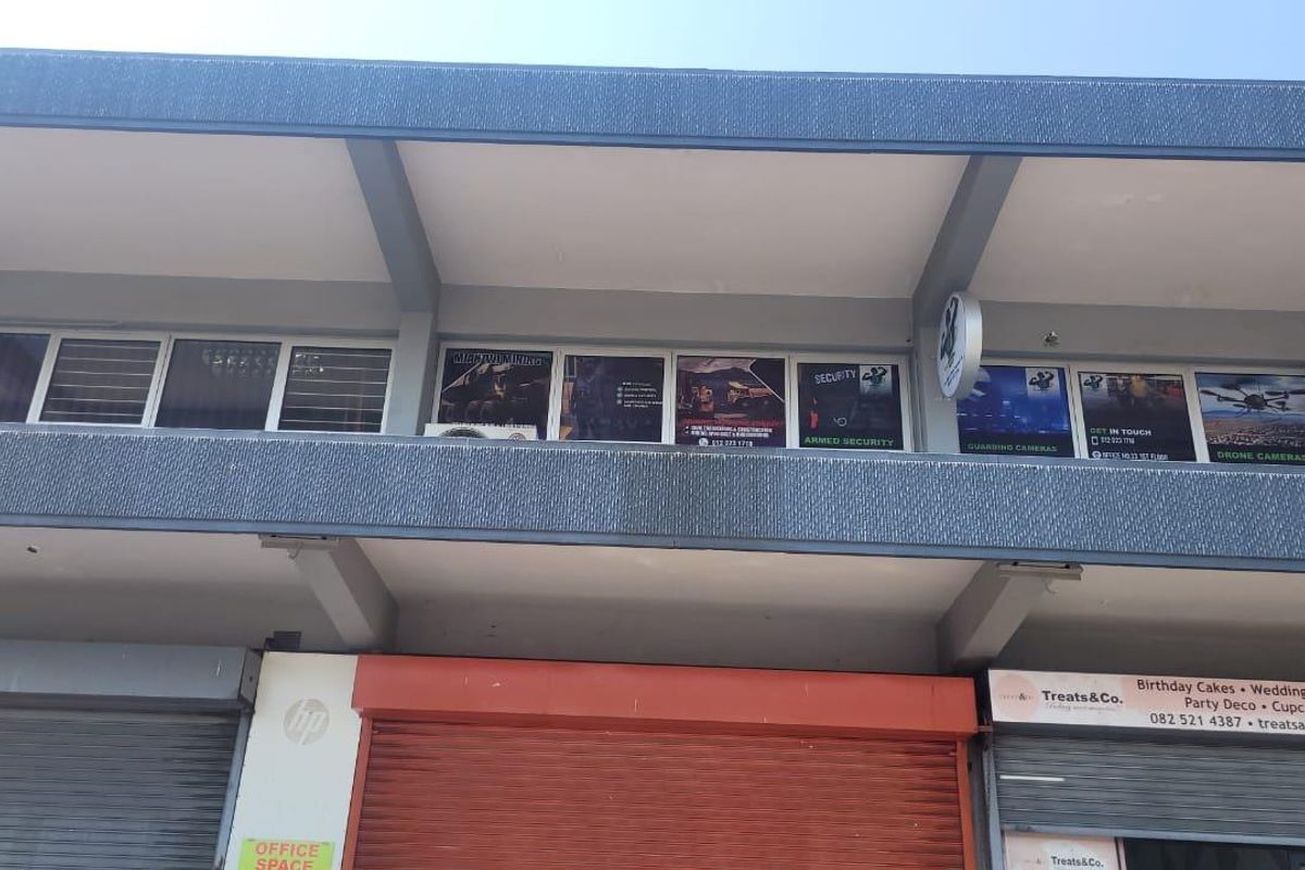 Front elevation of a commercial building featuring ground-level roller shutter doors and upper-level office windows with business signage.