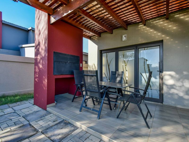 Covered patio area featuring a wooden pergola, built-in braai, and tiled flooring, providing direct access to the interior through sliding glass doors.