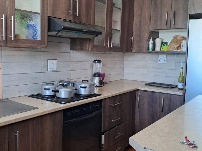 A functional kitchen featuring dark wood-finish cabinetry, laminate countertops, built-in oven, and hob, with tiled backsplash and flooring throughout.
