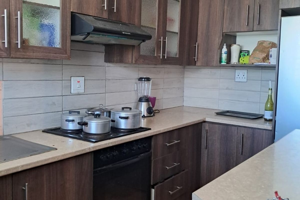 A functional kitchen featuring dark wood-finish cabinetry, laminate countertops, built-in oven, and hob, with tiled backsplash and flooring throughout.