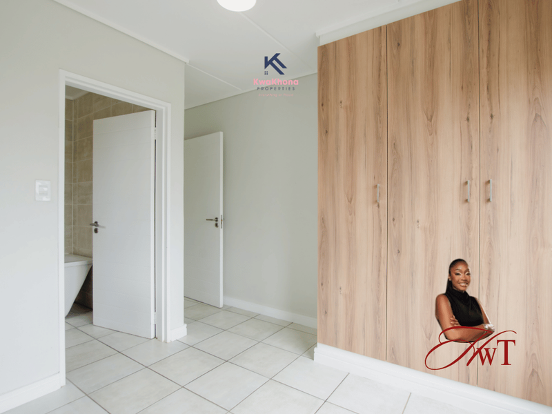 A clean, empty bedroom featuring light-toned built-in cupboards, neutral tiled flooring, and direct access to an en-suite bathroom.