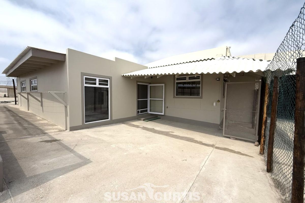 Rear exterior view of the property featuring a concrete patio area, covered veranda, and secure perimeter fencing.